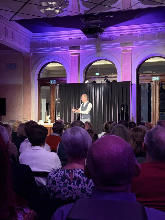 Solo-Performer auf der Atrium-Bühne, violettes Licht, Publikum im Vordergrund